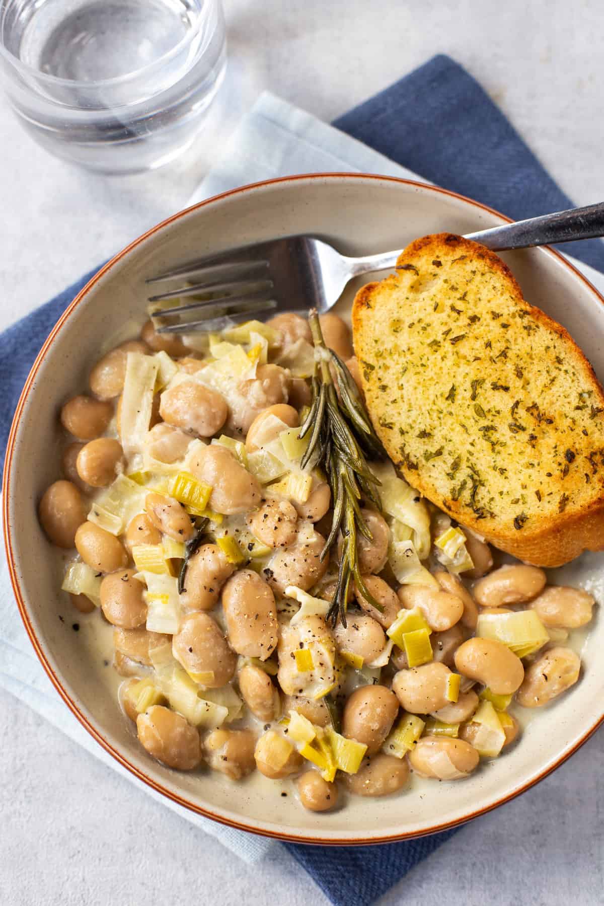 Overhead shot of a bowl of creamy butter beans served with garlic bread.