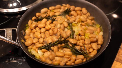 A frying pan with butter beans and fresh rosemary.