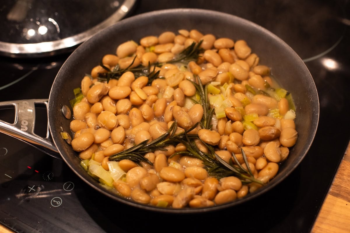 A frying pan with butter beans and fresh rosemary.