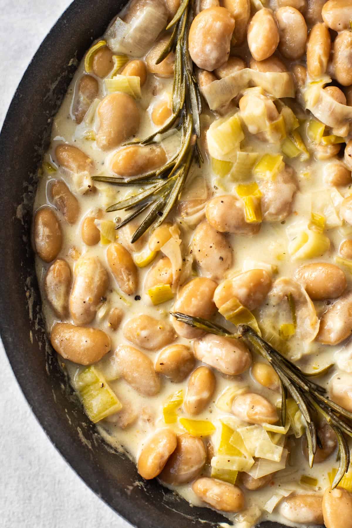 Close up shot of creamy butter beans in a frying pan with leeks and rosemary.