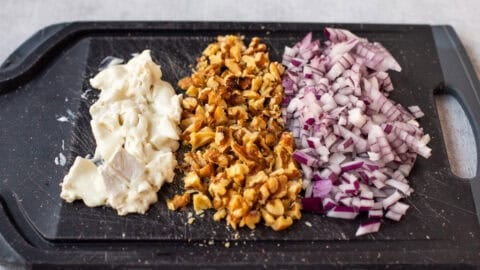 Chopped goat cheese, walnuts and red onion on a cutting board.