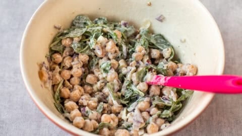 A mixing bowl filled with creamy chickpea salad with goat cheese and arugula.