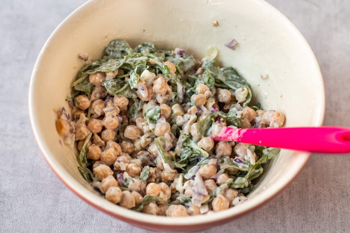 A mixing bowl filled with creamy chickpea salad with goat cheese and arugula.