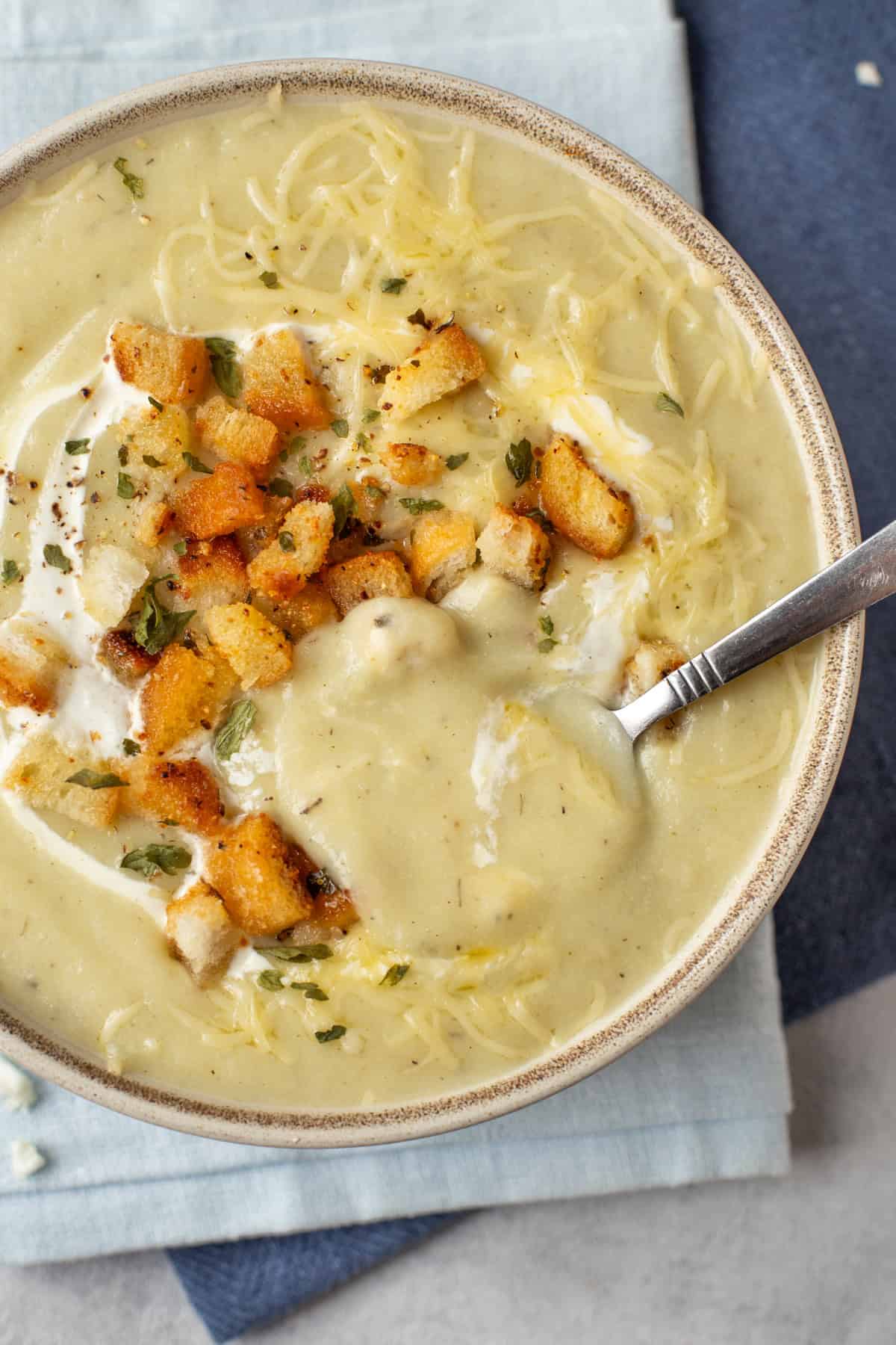 A spoon taking a scoop from a bowl of cheesy cauliflower soup.