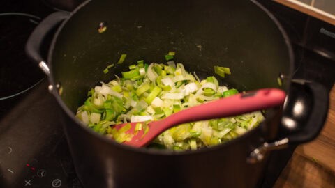 Sliced leeks being sautéed in a large saucepan.