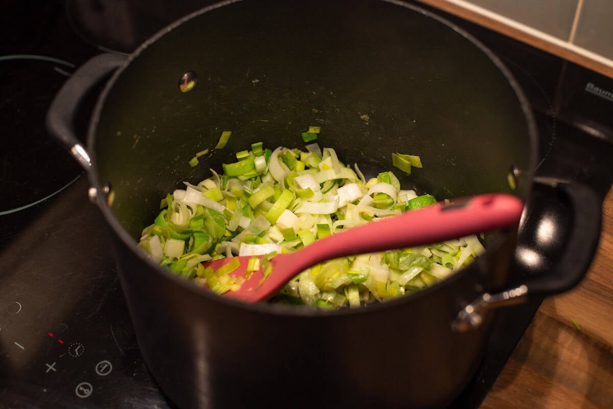 Sliced leeks being sautéed in a large saucepan.