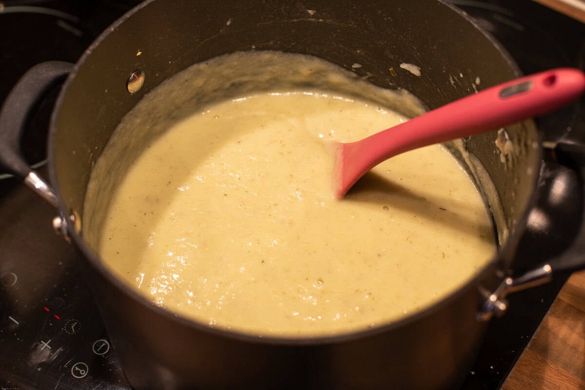 Creamy cauliflower cheese soup in a large saucepan with a pink spoon.