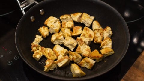 Crispy tofu pieces cooking in a frying pan.