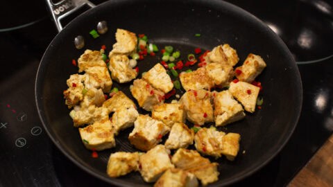 Crispy tofu cooking in a frying pan with chilli and spring onions.