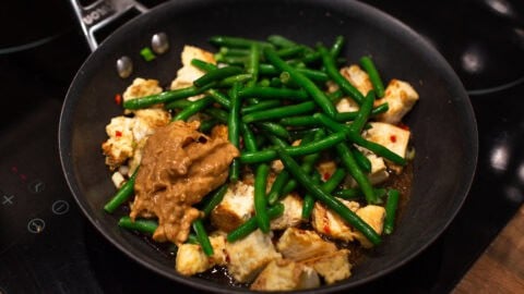 Green beans and peanut butter with tofu in a frying pan.