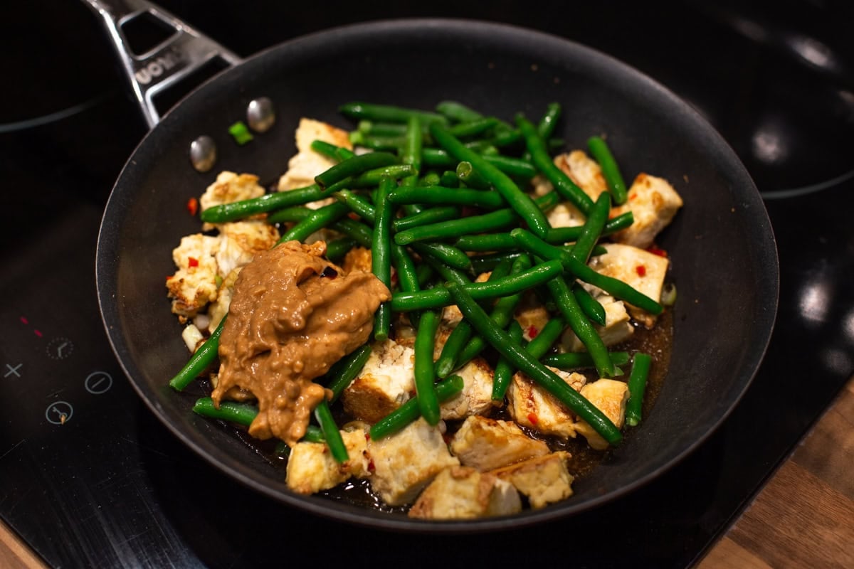 Green beans and peanut butter with tofu in a frying pan.