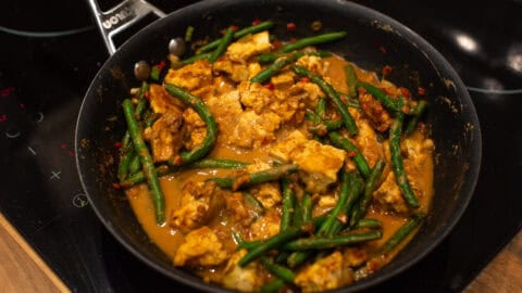 Peanut butter tofu and green beans cooking in a frying pan.