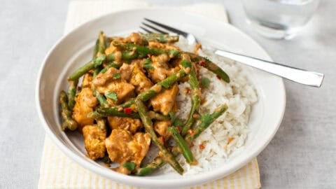 Portion of creamy peanut butter tofu and green beans in a bowl with rice.