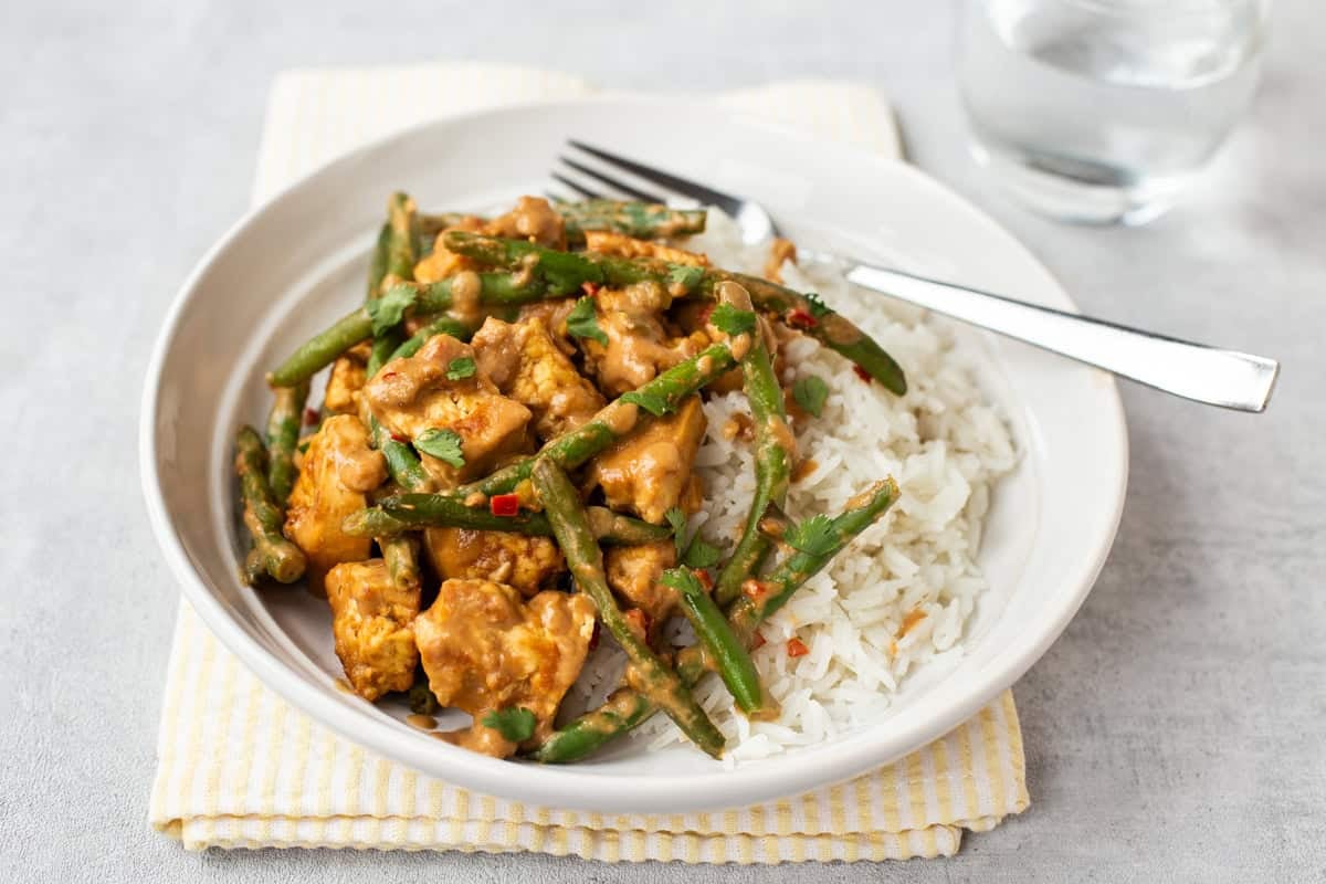 Portion of creamy peanut butter tofu and green beans in a bowl with rice.