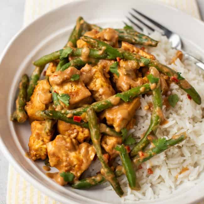 A portion of creamy peanut butter tofu with green beans in a bowl with rice.