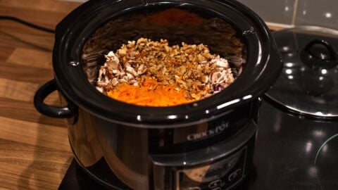 A slow cooker filled with chopped vegetables and walnuts.