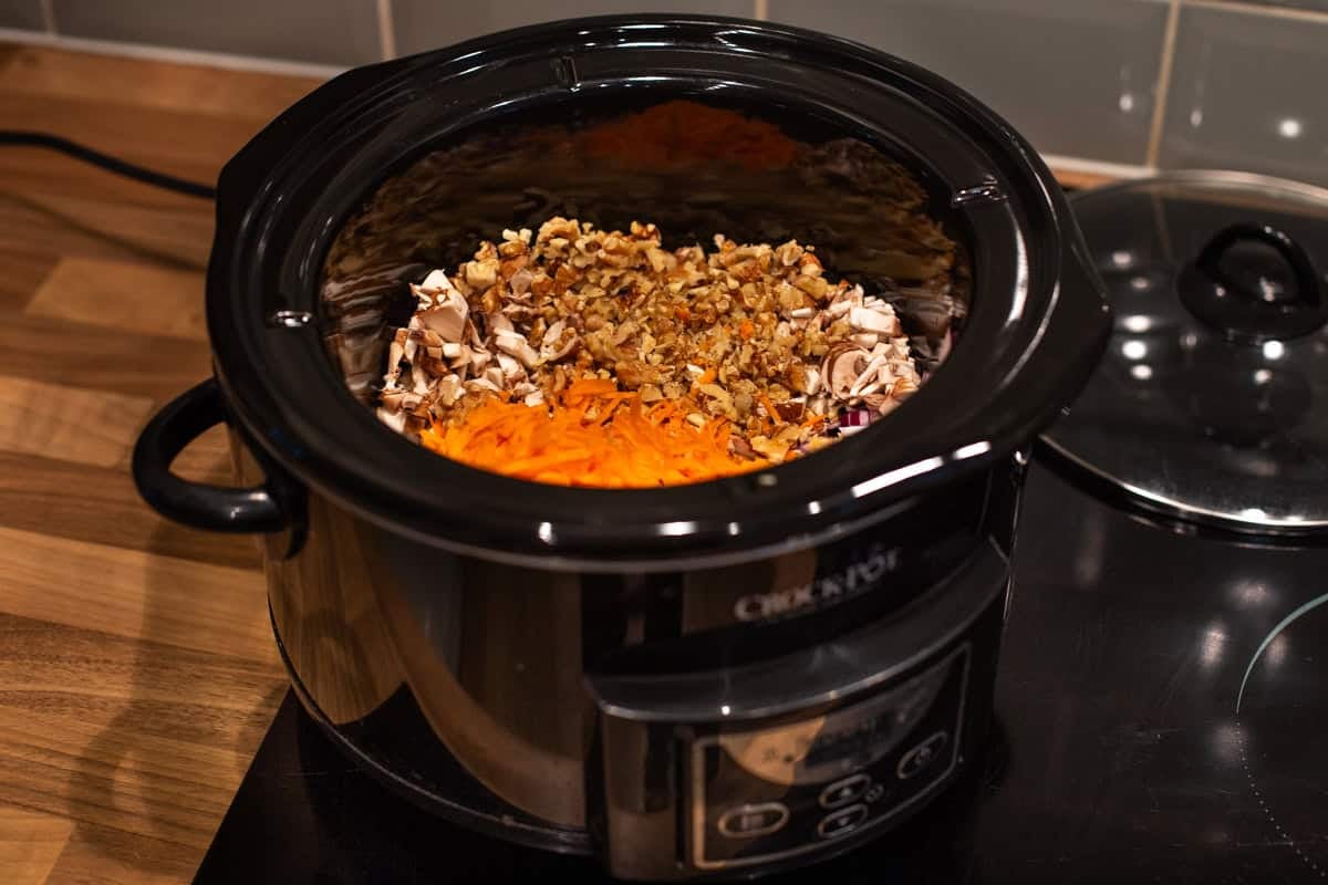A slow cooker filled with chopped vegetables and walnuts.
