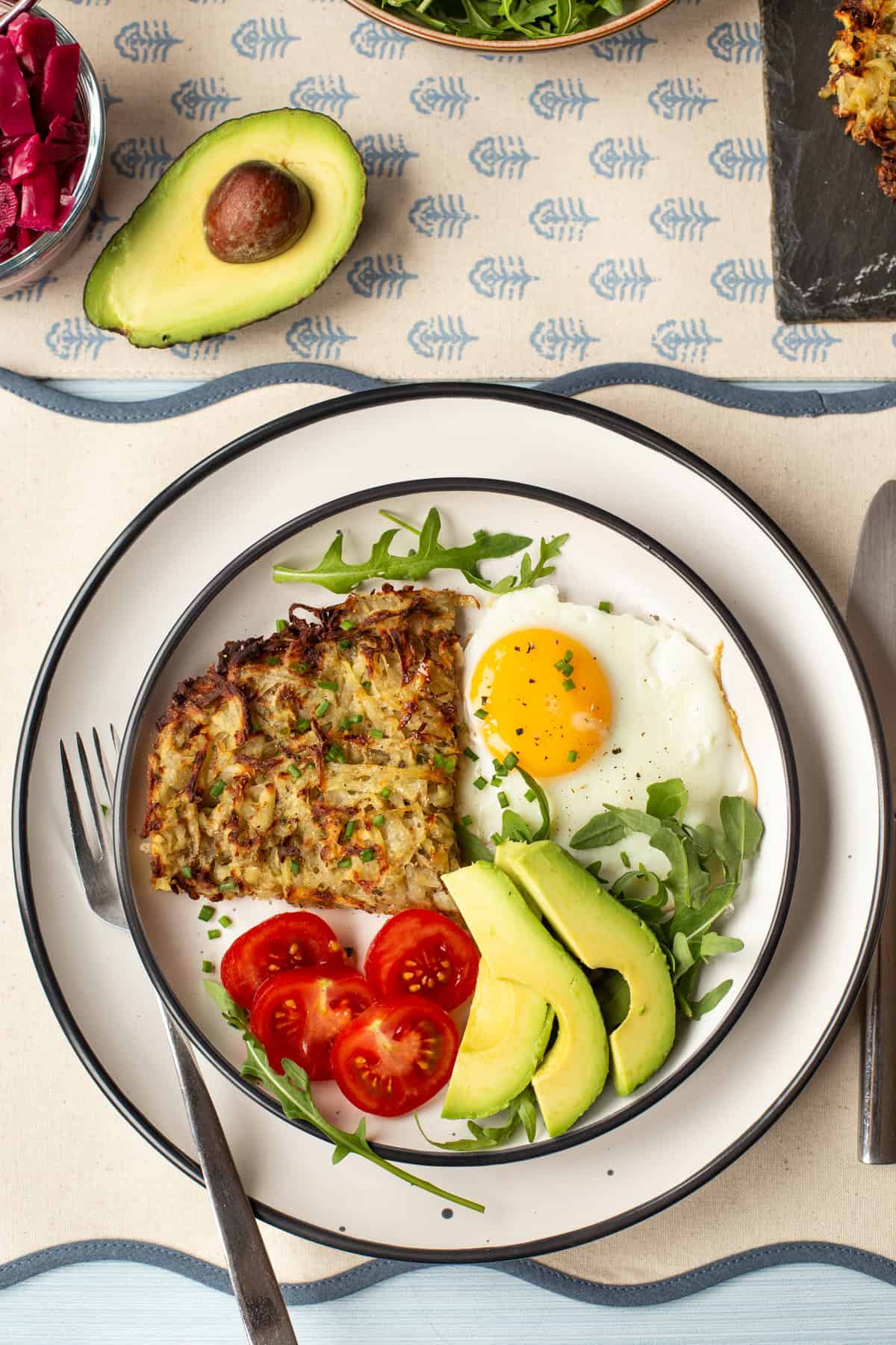 Overhead shot of a portion of air fryer hash browns on a plate with a fried egg, tomatoes and avocado.