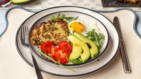 A portion of air fryer hash browns on a plate with a fried egg, tomatoes and avocado.