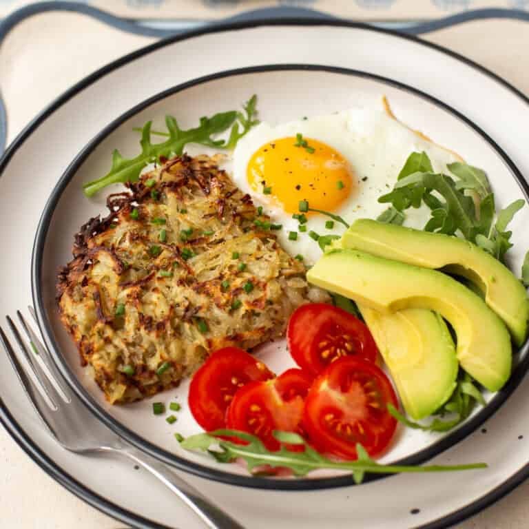 A portion of air fryer hash browns on a plate with a fried egg, tomatoes and avocado.