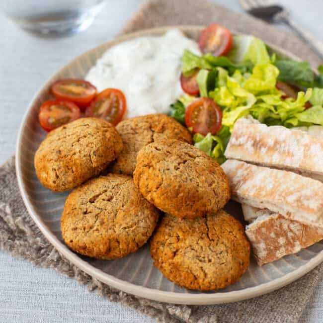A few pieces of falafel on a plate with pitta bread, salad and tzatziki.
