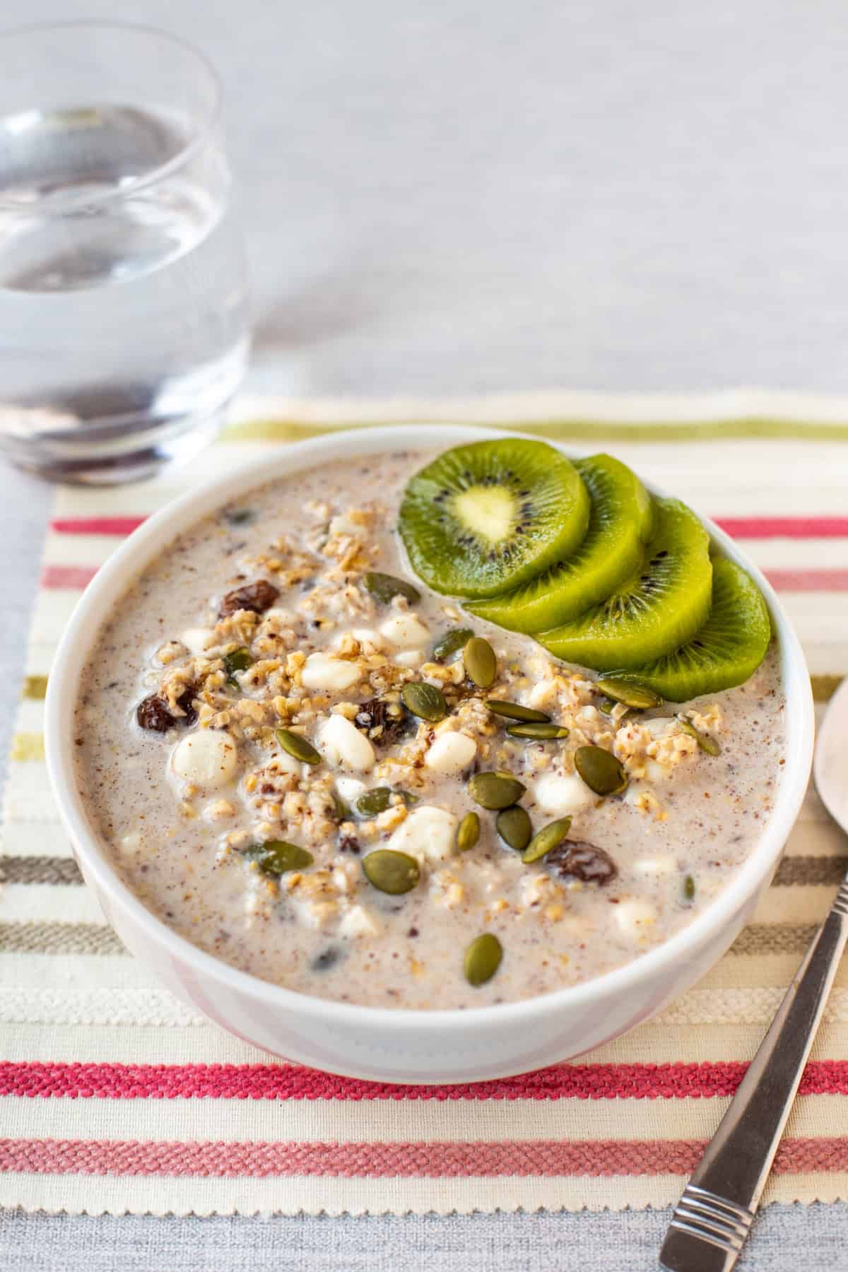 A bowl of high protein overnight oats topped with sliced kiwi and pumpkin seeds.