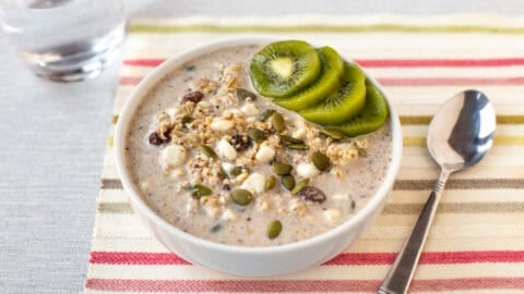 A bowl of high protein overnight oats topped with sliced kiwi and pumpkin seeds.