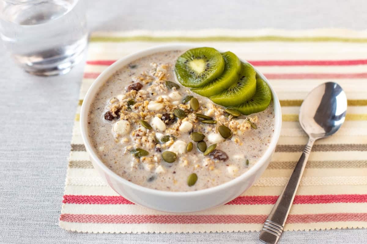 A bowl of high protein overnight oats topped with sliced kiwi and pumpkin seeds.
