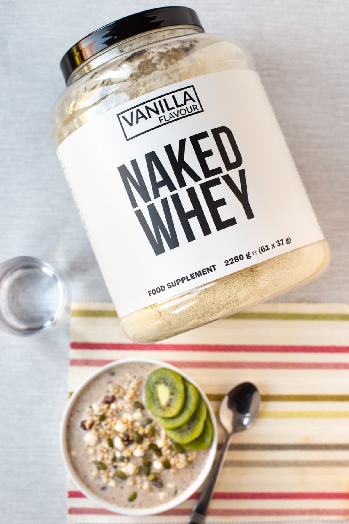 A large tub of vanilla whey protein powder with a bowl of overnight oats.