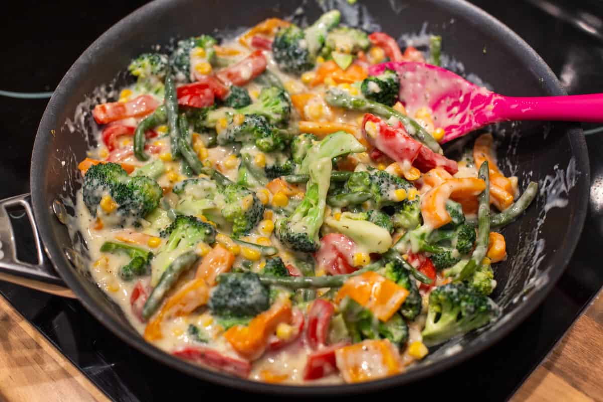 Vegetables in a creamy sauce in a frying pan.