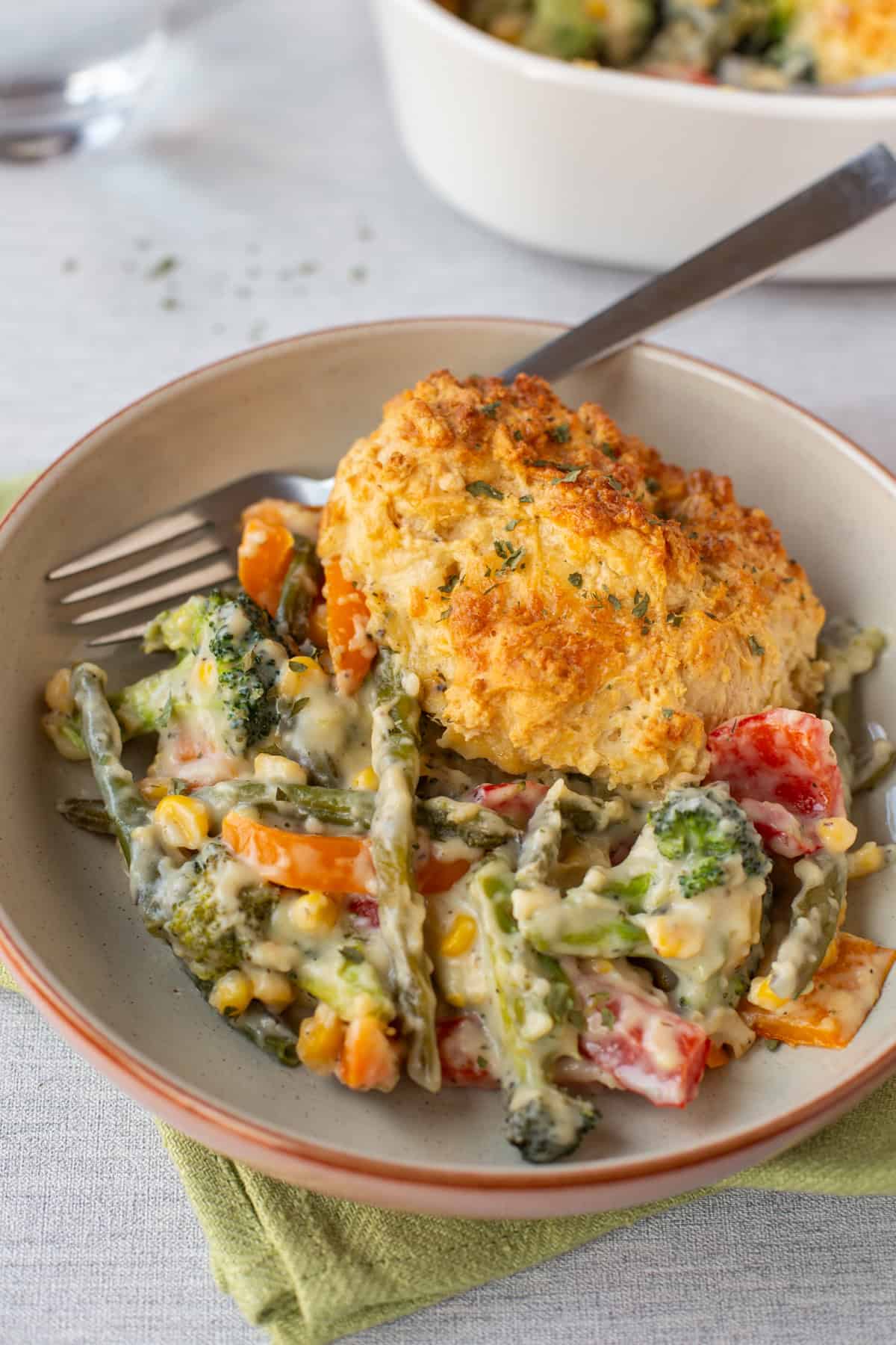 A portion of vegetable cobbler in a bowl with a cheesy scone.