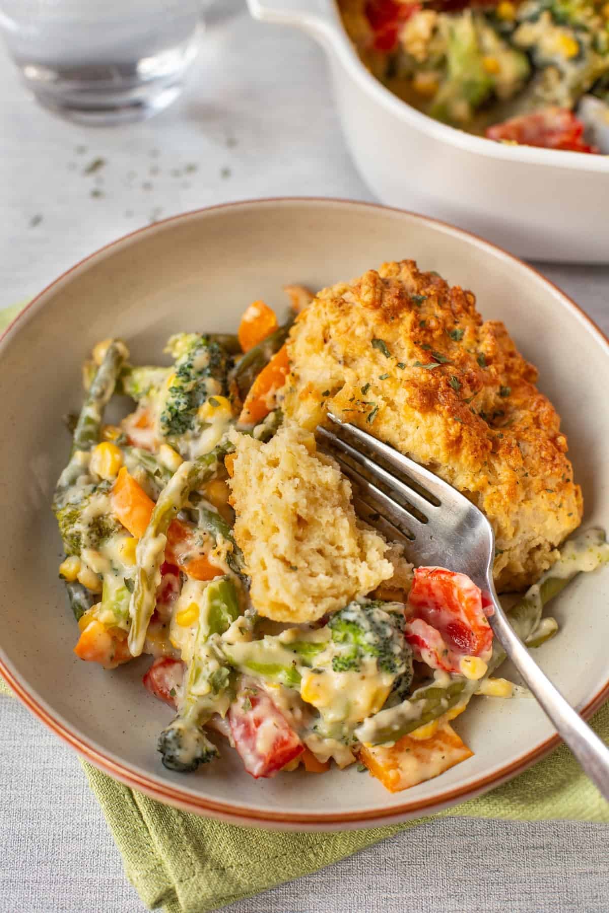 A fork cutting a piece of cheese scone on top of some creamy vegetables.