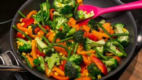 Mixed vegetables cooking in a large frying pan.