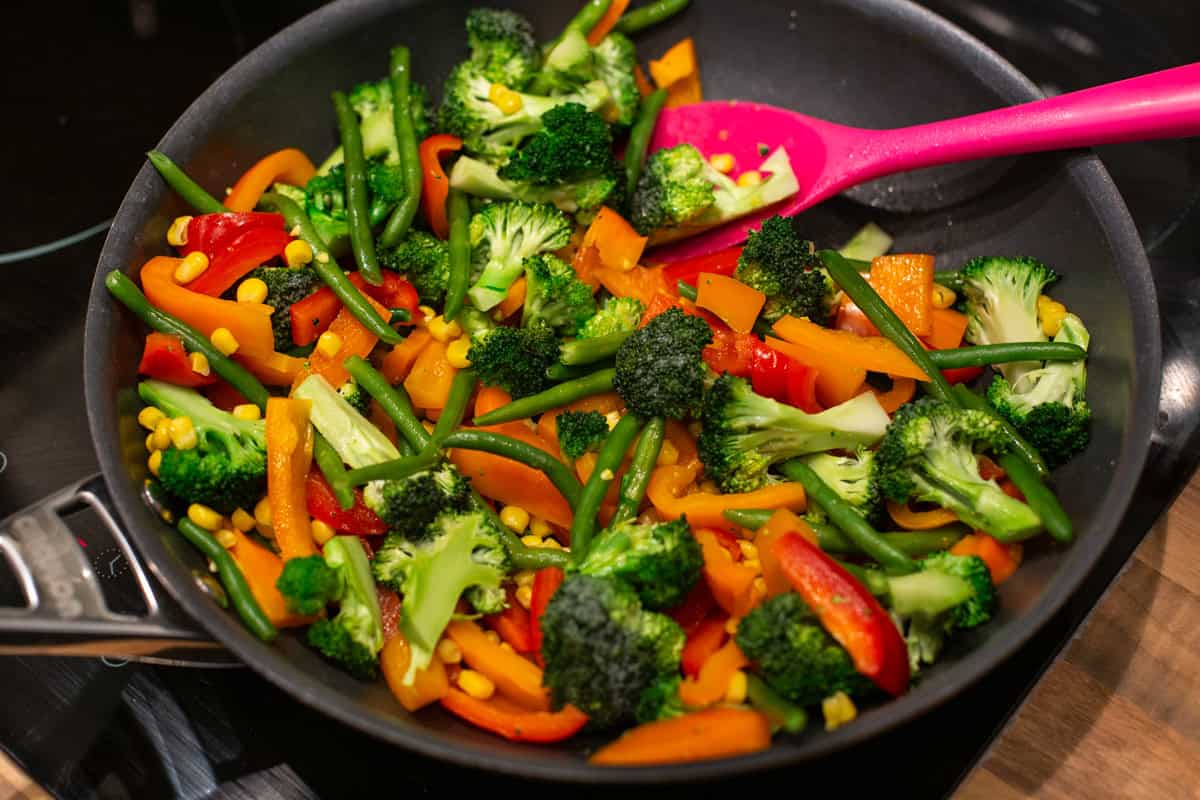 Mixed vegetables cooking in a large frying pan.