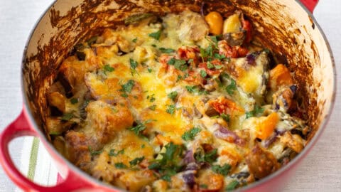 A big pot of cheesy vegetable potato bake topped with fresh herbs.