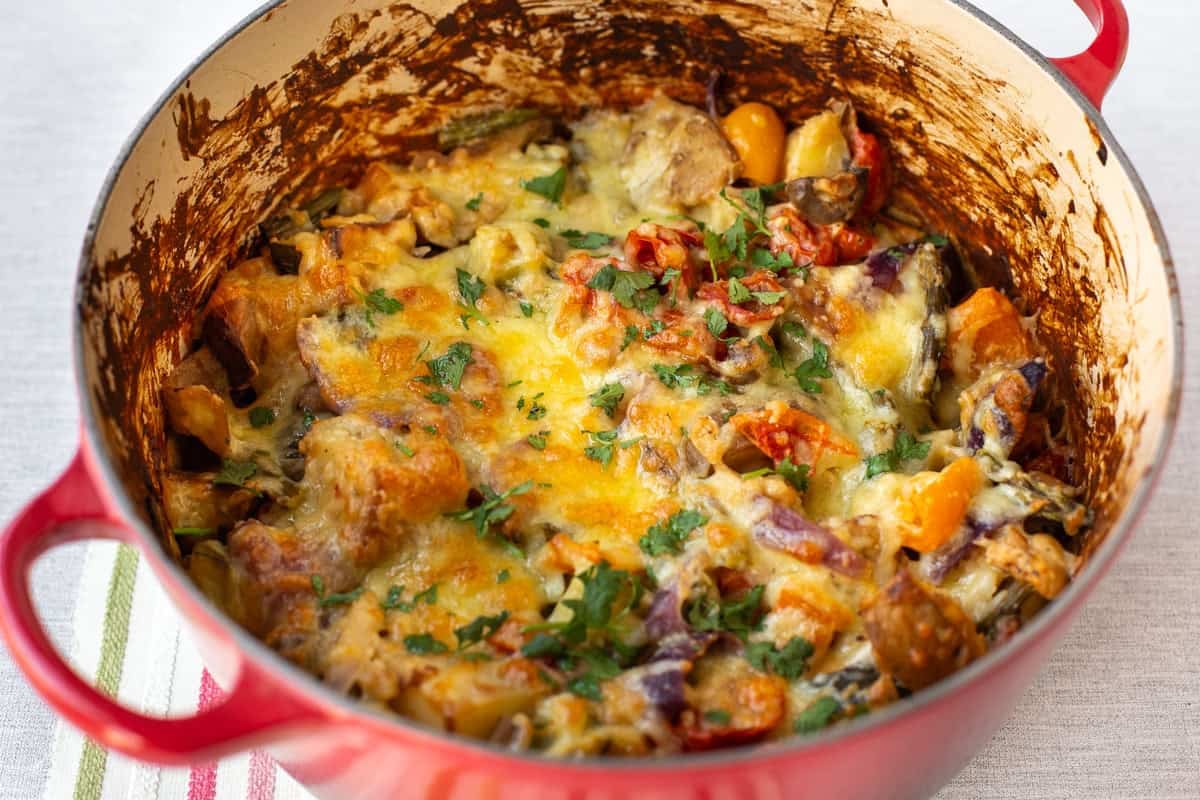 A big pot of cheesy vegetable potato bake topped with fresh herbs.