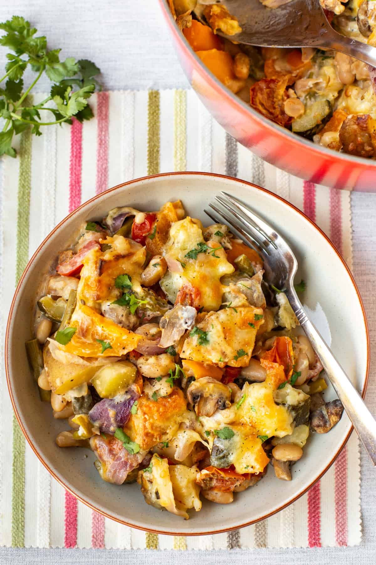 A portion of cheesy vegetable potato bake in a bowl with a fork.