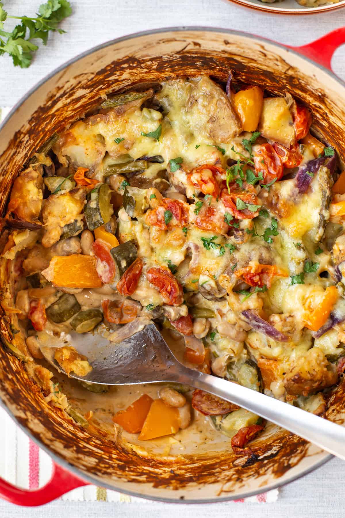 Overhead shot of cheesy vegetable potato bake in a large pot with a spoonful scooped out.