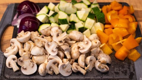 Chopped vegetables (red onion, zucchini, pepper, mushrooms) on a cutting board.