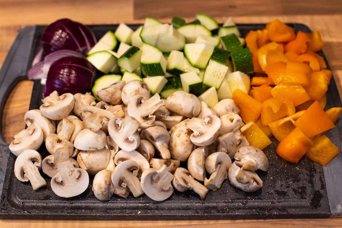 Chopped vegetables (red onion, zucchini, pepper, mushrooms) on a cutting board.