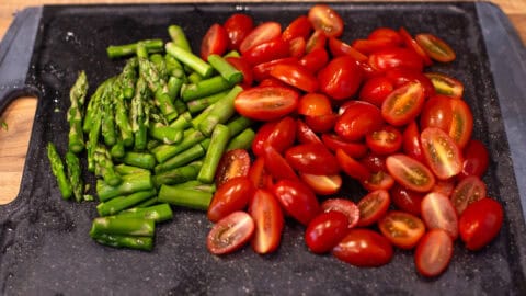 Chopped asparagus and cherry tomatoes on a cutting board.