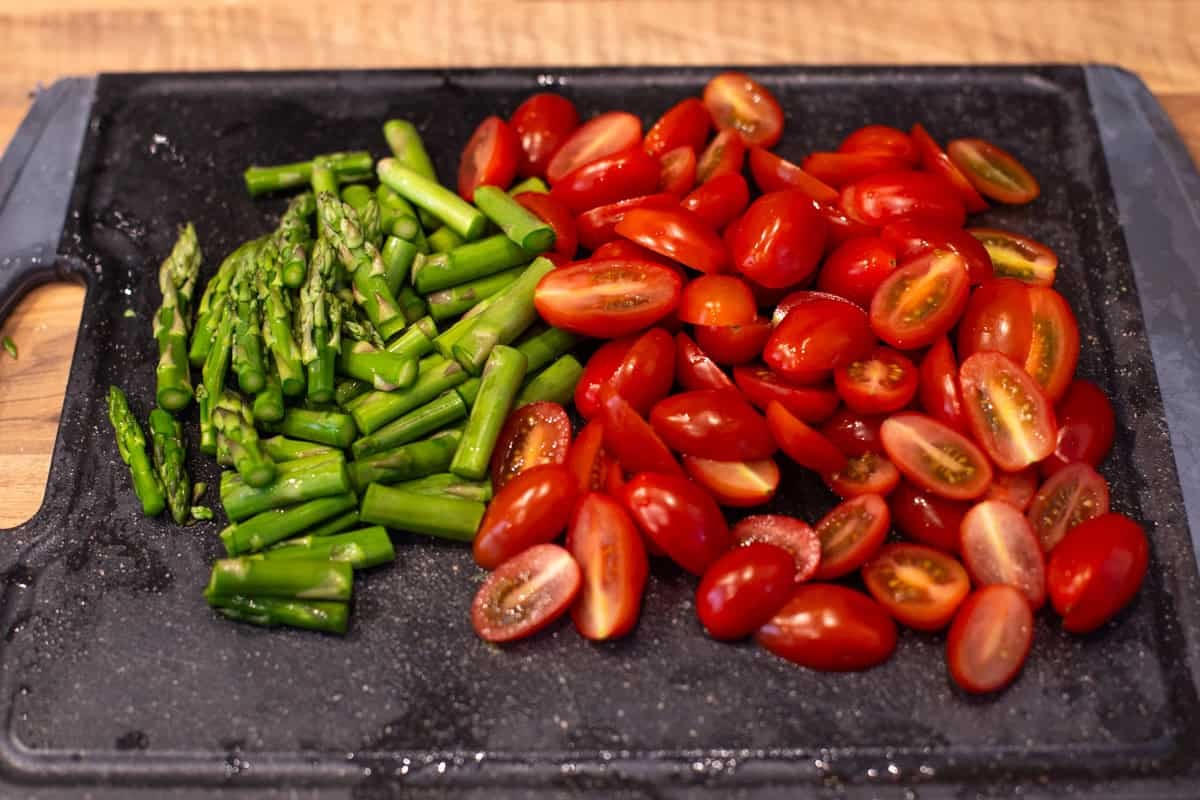 Chopped asparagus and cherry tomatoes on a cutting board.