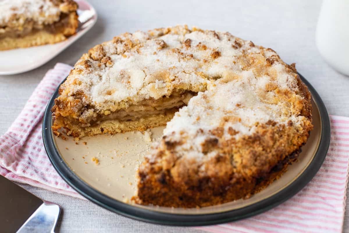 An easy apple crumble cake on a plate with a slice removed.