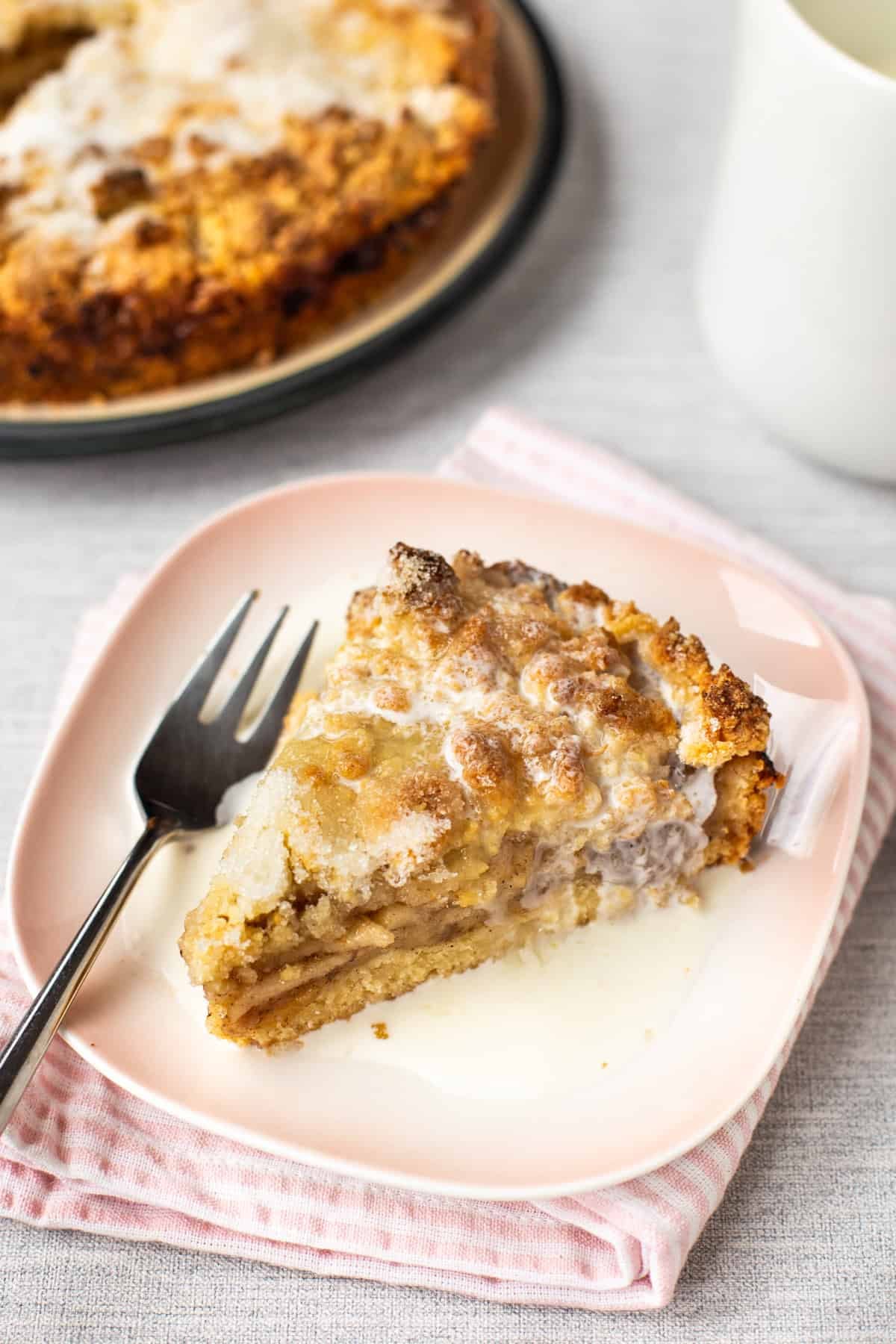 A slice of easy apple crumble cake on a plate with cream.