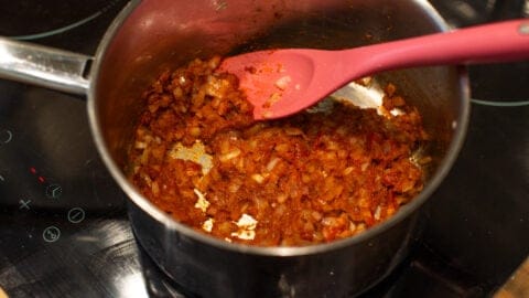 Diced onions, tomato paste and spices cooking in a saucepan.