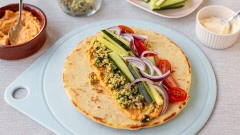 A flatbread laid on a board topped with hummus, tabbouleh and vegetables.