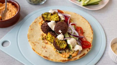 Tabbouleh and falafel wrap on a board with raw vegetables and hummus.