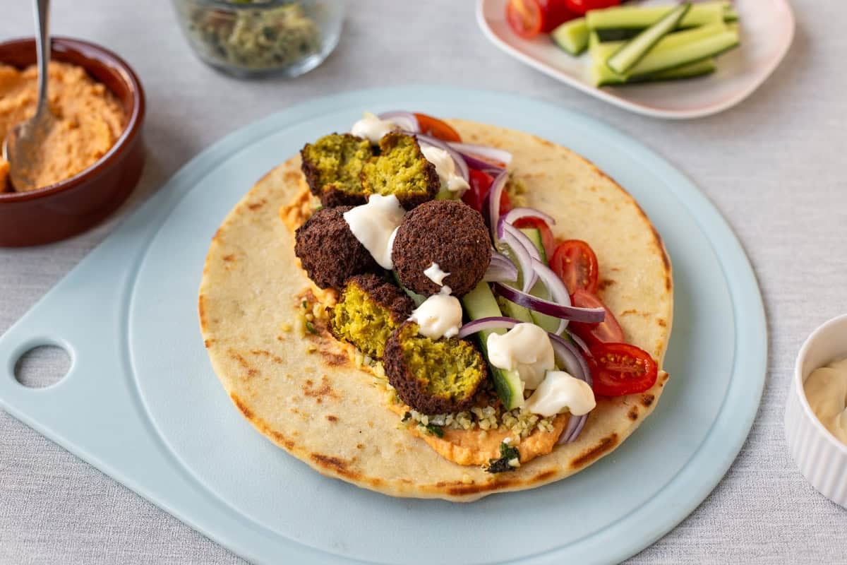 Tabbouleh and falafel wrap on a board with raw vegetables and hummus.