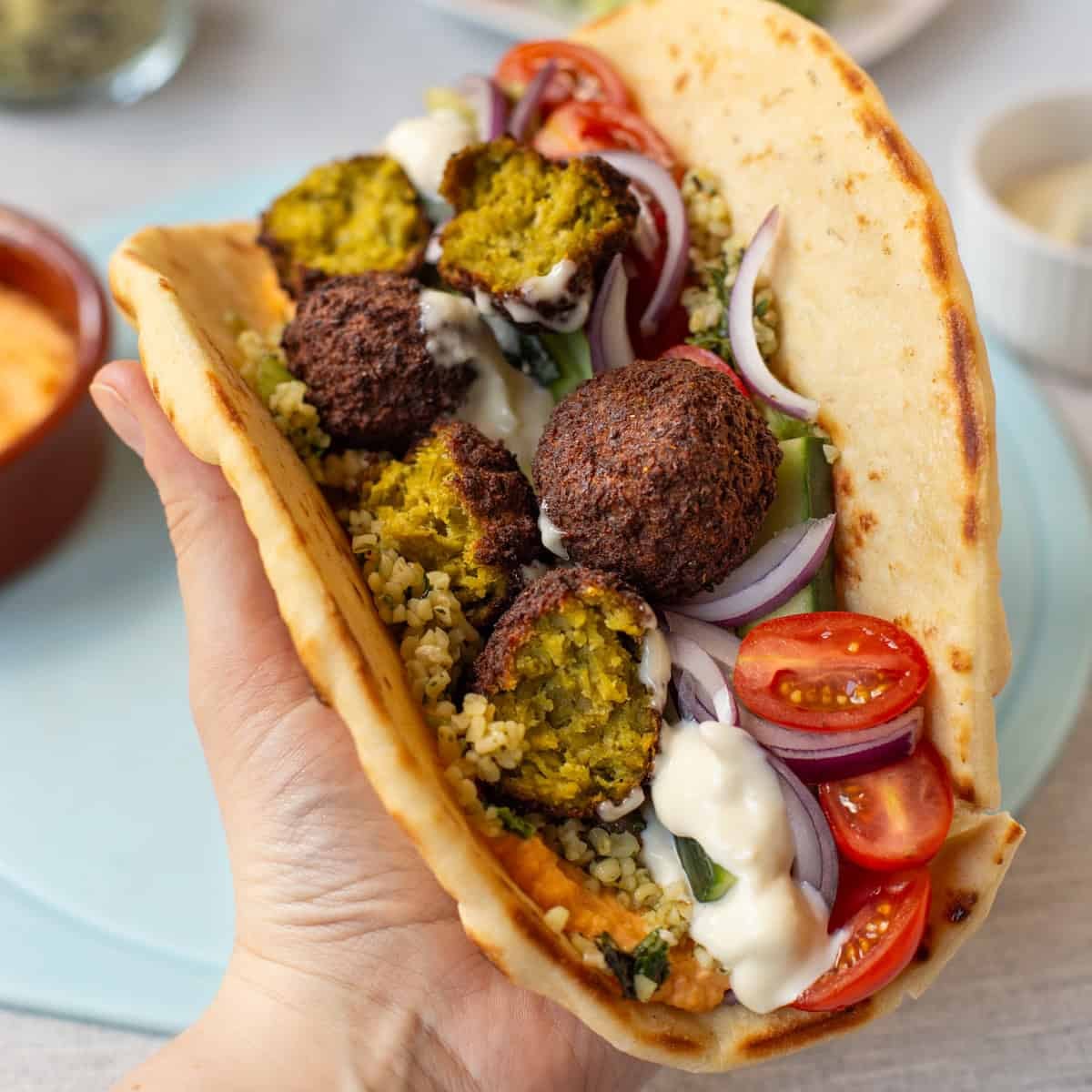 A hand holding a falafel and tabbouleh wrap.