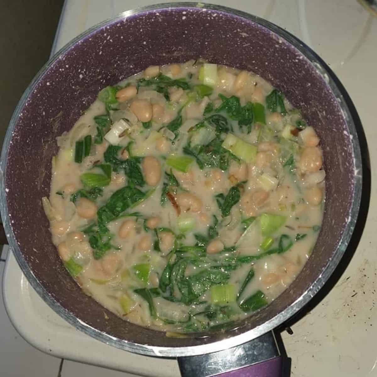 Creamy white beans with green vegetables in a frying pan.